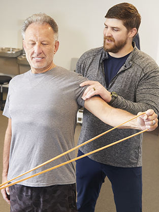 A man doing arm workouts using a resistance band with guidance from his physical therapist.