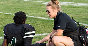Athletic trainer kneeling beside an injured player on a football field.