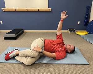 Man lying on his side with knees bent for a stretch and raising his arm toward the ceiling.