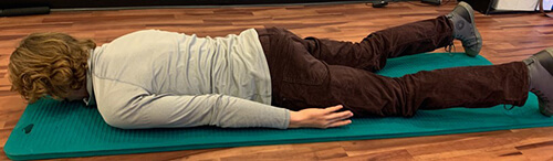 Man lying face down on an exercise mat with arms stretched behind at his sides.