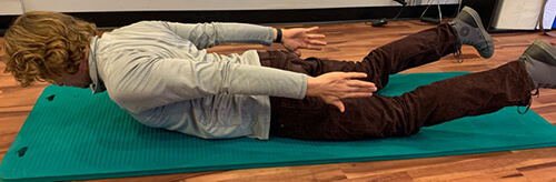 Man lying on his stomach on an exercise mat and lifting head and feet with arms stretched behind at his sides.