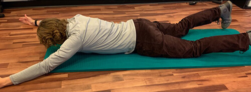 Man lying face down on an exercise mat with arms stretched out in front of his body.