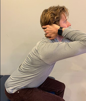 Man using hands placed behind his neck to pull head forward in a stretch.