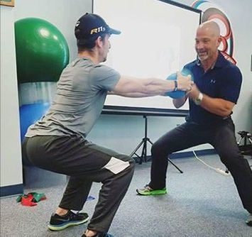 Patient and male therapist in squat position tugging back and forth on a small blue ball.
