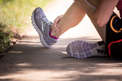 Female runner sitting on sidewalk holding her ankle.