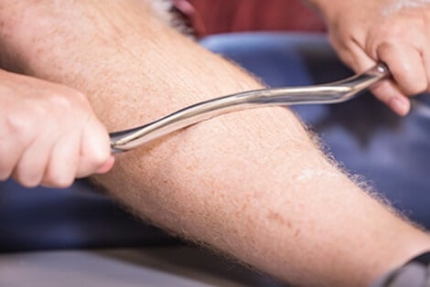 IASTM tool being applied to a man's calf muscle.