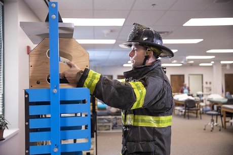 Man wearing firefighting gear and helmet reaching up to place a box on a shelf.