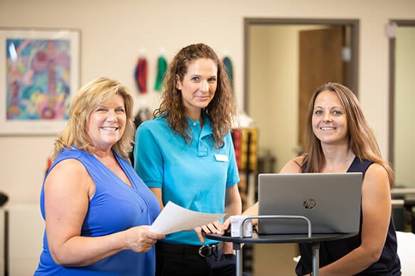 Three female therapists standing next to a rolling desk and using a laptop.