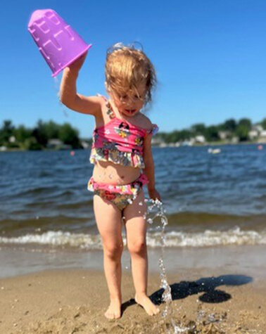 Charlie in a bathing suit at the beach dumping water from a bucket