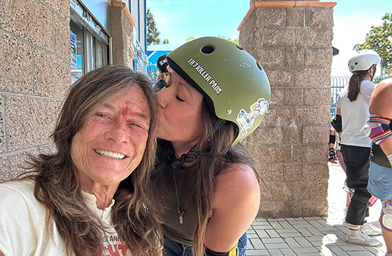 Jess with a helmet on kissing Tracie's cheek while Tracie is smiling at the camera